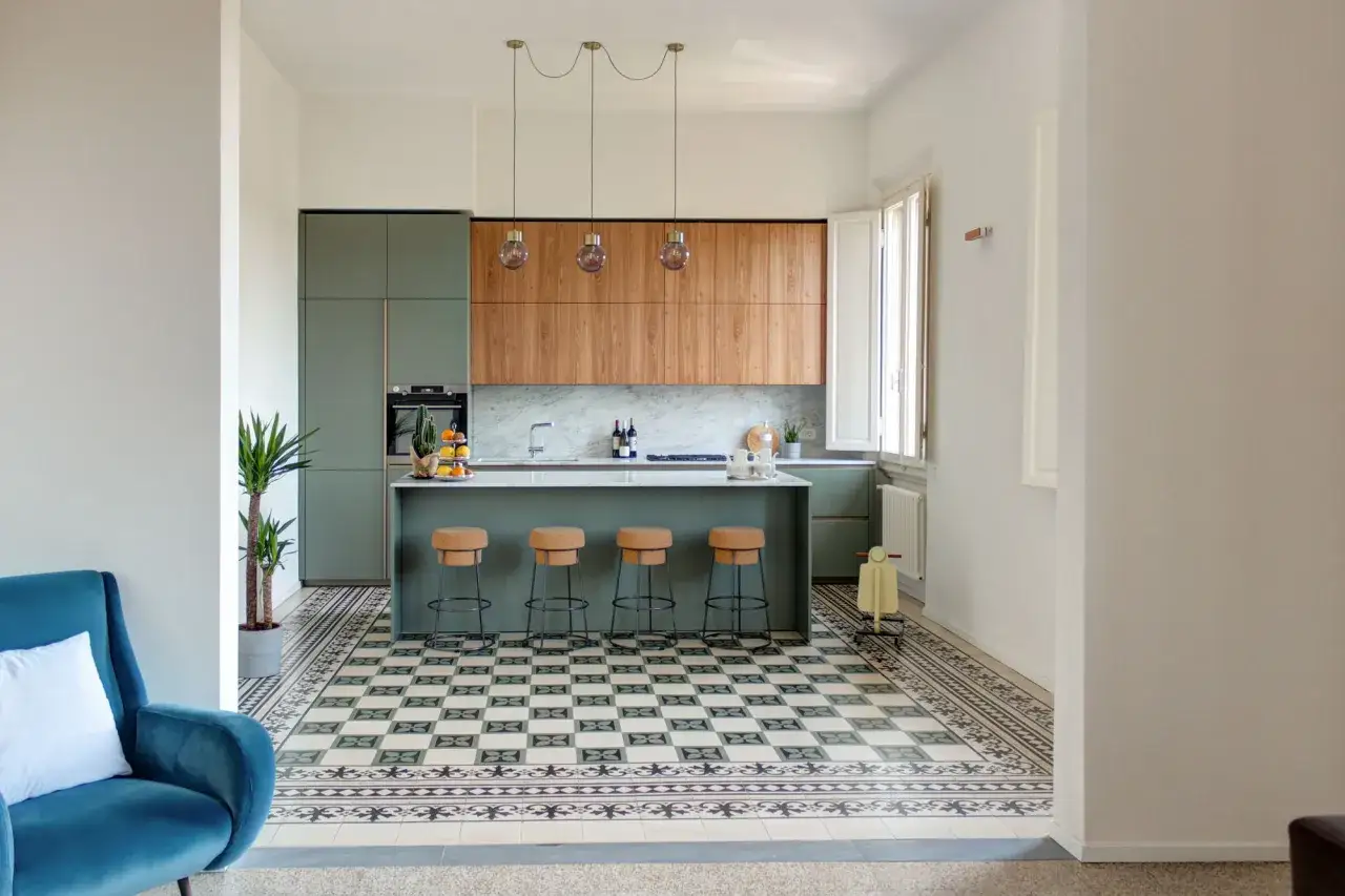 Cucina moderna con isola centrale, sgabelli in sughero e un mix di parquet e cementine decorative sul pavimento.