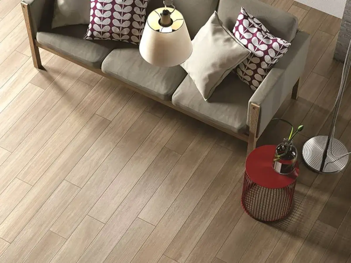 Schemi posa piastrelle rettangolari effetto legno chiaro, con divano grigio e tavolino rosso.