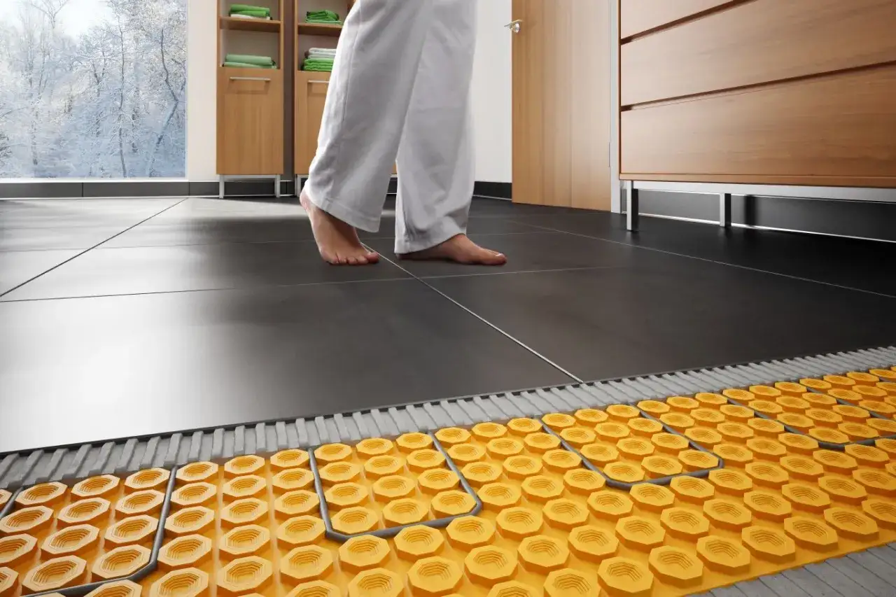 Piedi nudi su piastrelle scure, con vista su un sistema di riscaldamento a pavimento giallo sottostante. Comfort e calore in inverno.