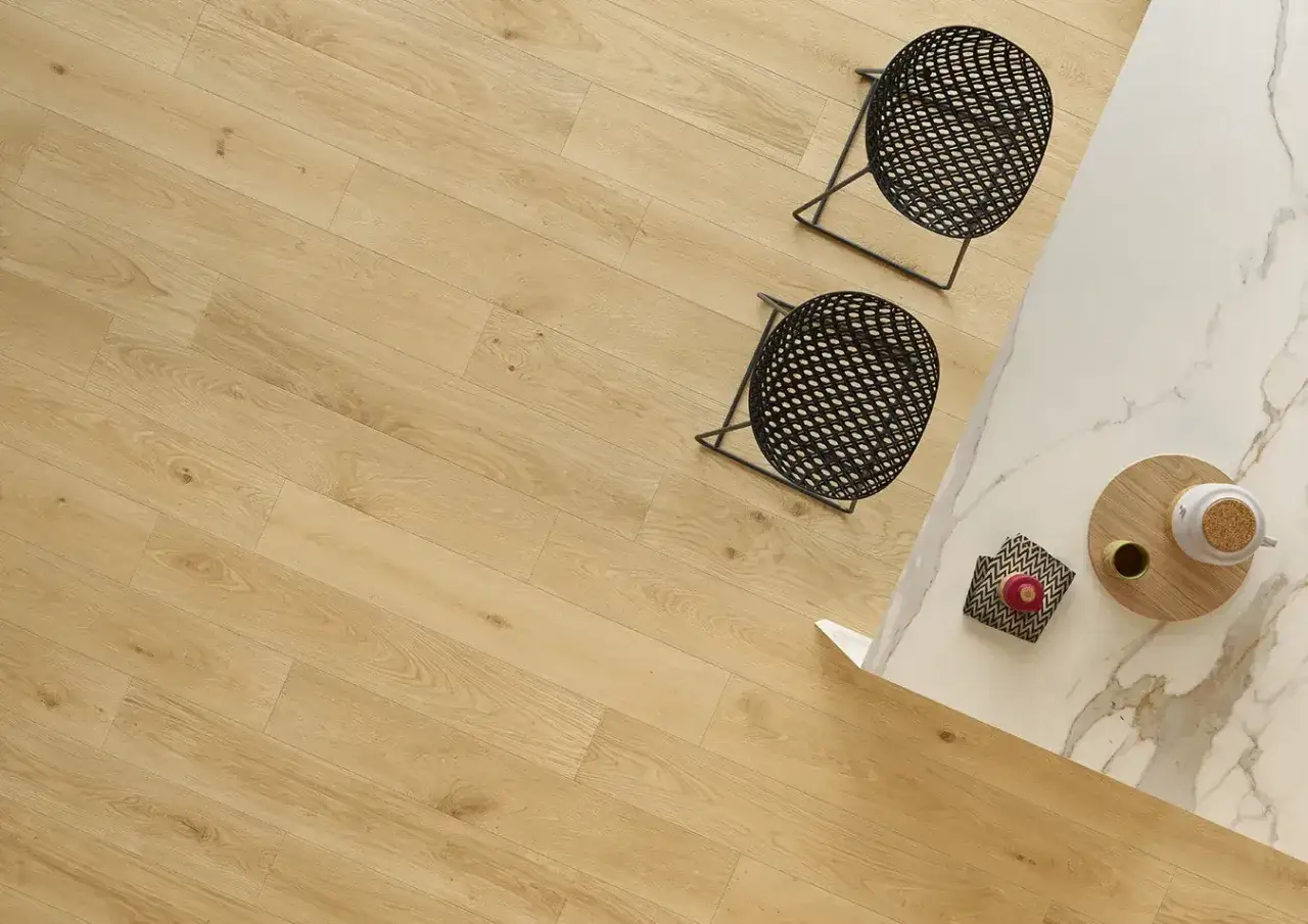 Un angolo cucina moderno con pavimento effetto legno chiaro, sgabelli neri e piano in marmo. Si può posare gres su parquet per un look simile.