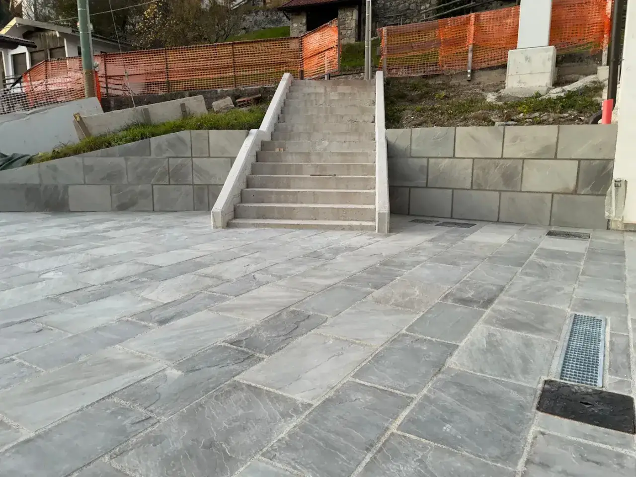 Piattaforma pavimentata con lastre di klinker grigio, con gradinata in cemento e muro di contenimento in pietra grigia.