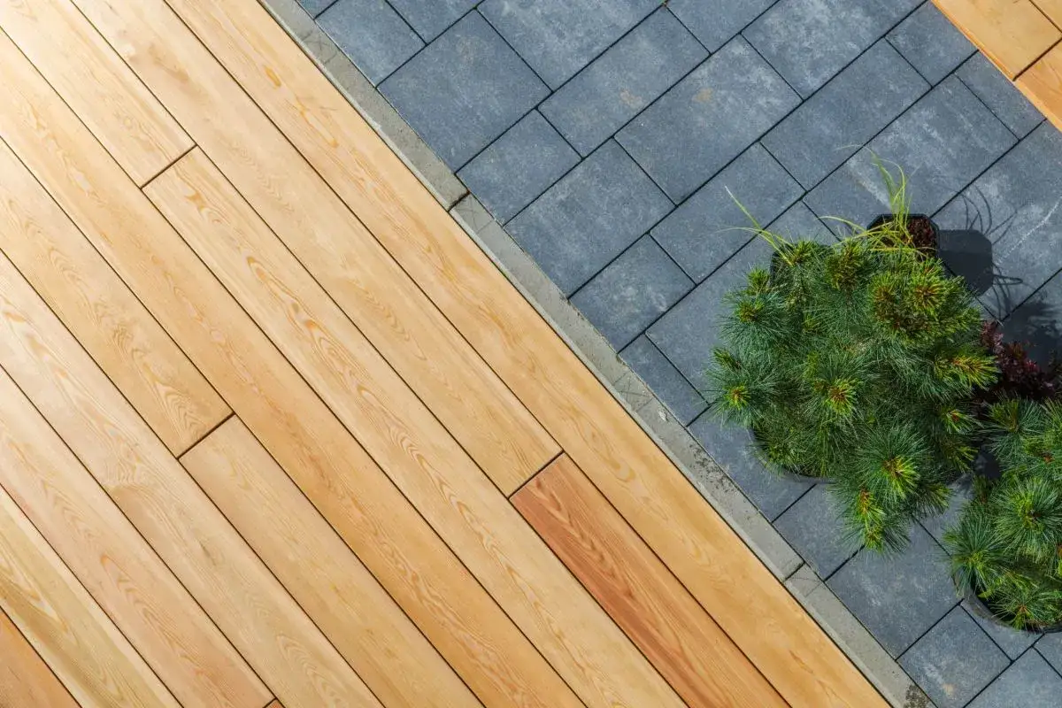 Posa in opera di pavimenti per esterni carrabili in legno e pietra scura, con aiuole di pini nani.