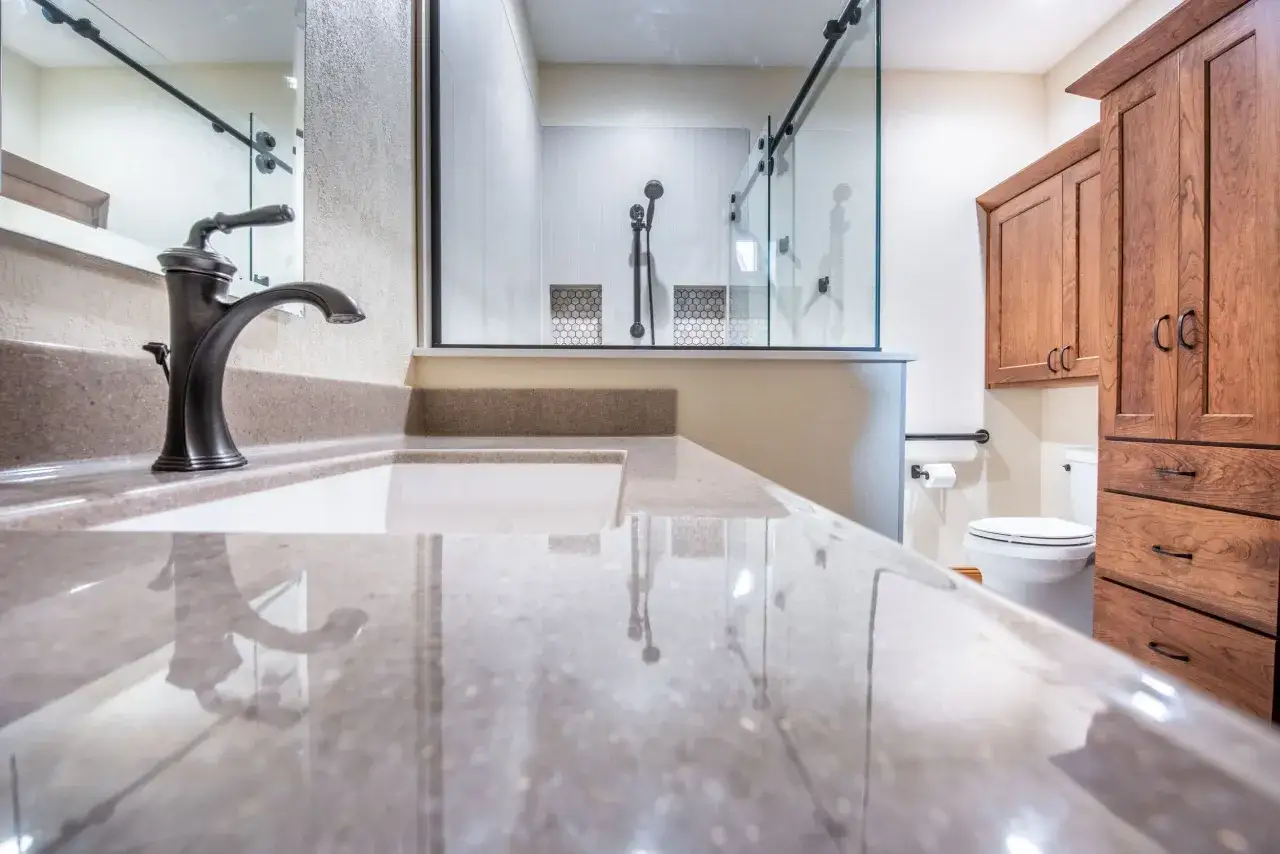 Bagno moderno con lavabo in quarzo lucido, doccia a vista e mobili in legno. Il pavimento facile da pulire completa l'ambiente.