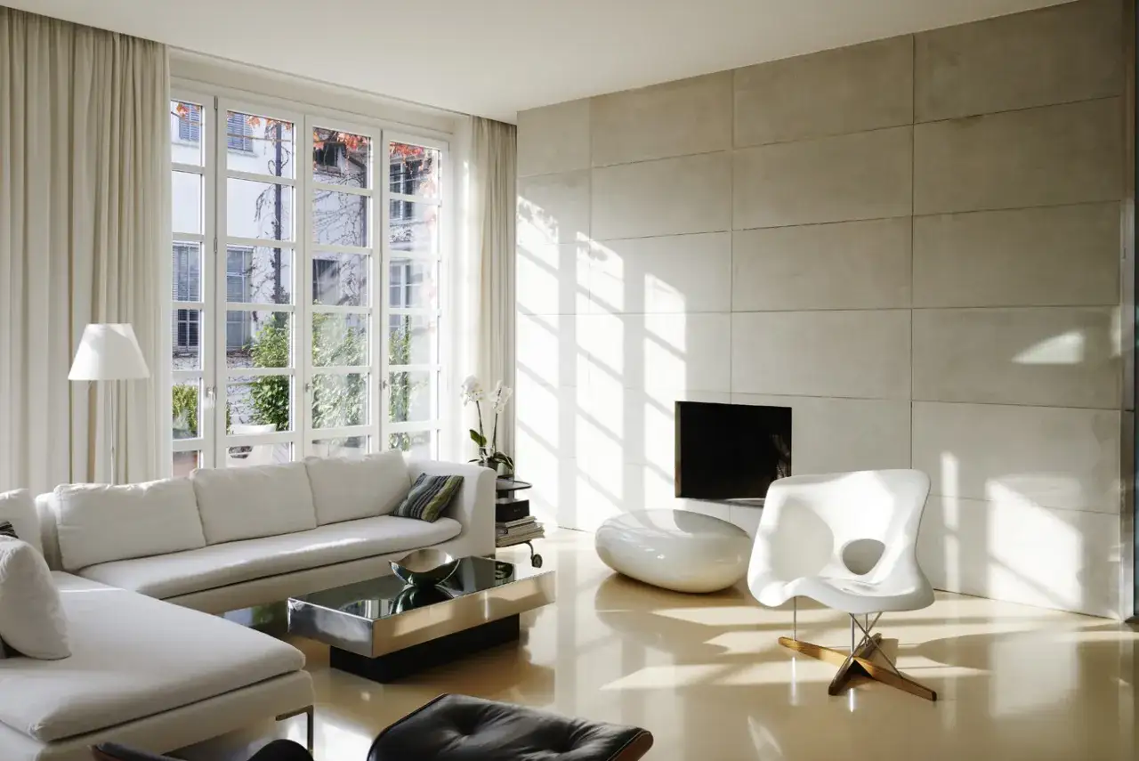 Soggiorno moderno con divano bianco, tavolino di design e camino. Pavimenti e rivestimenti in resina creano un ambiente luminoso e continuo.