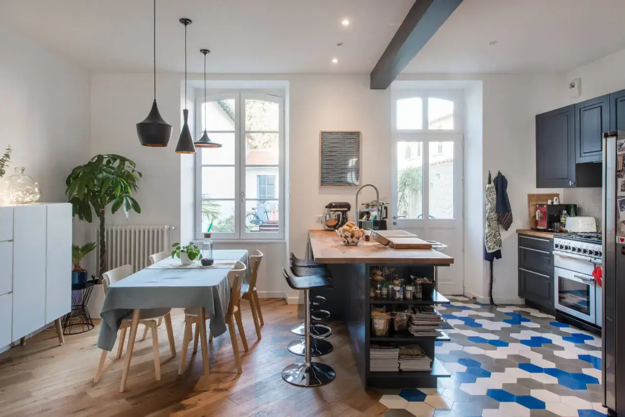 Cucina moderna con pavimenti in parquet e cementine esagonali. Tavolo apparecchiato, isola con sgabelli e cucina a vista.