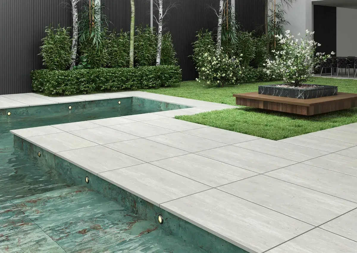 Pavimentazione terrazzo moderna con piscina e giardino curato. Le lastre grigie creano un percorso elegante attorno all'acqua.