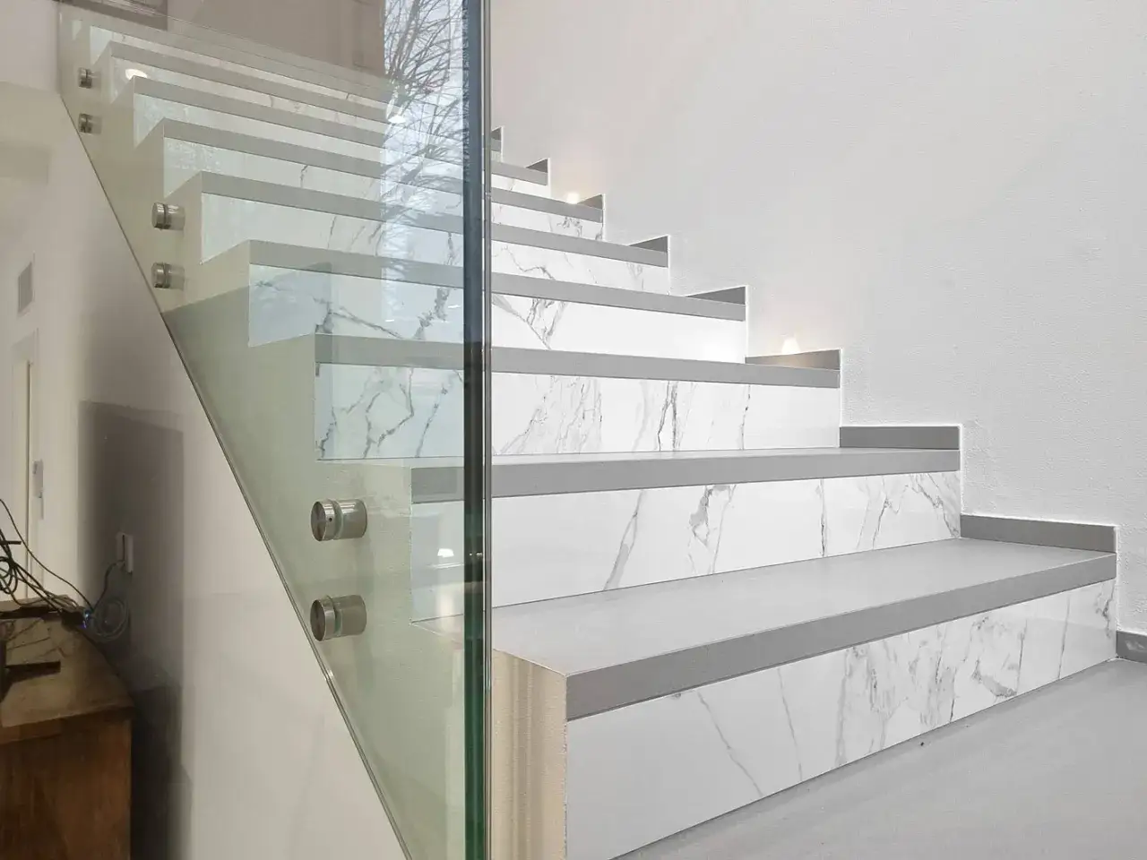 Elegante scala con gradini in gres porcellanato effetto marmo bianco e grigio, protetta da un parapetto in vetro.