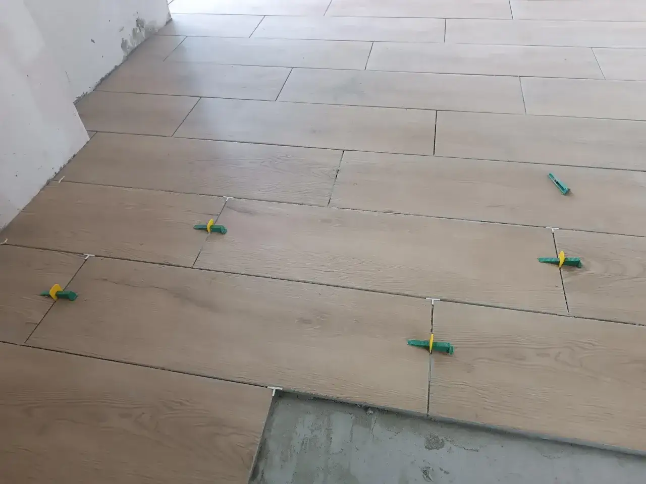 Posa di piastrelle effetto legno con distanziatori verdi. Ottenere preventivi per i prezzi piastrellista al mq è fondamentale per un lavoro ben fatto.