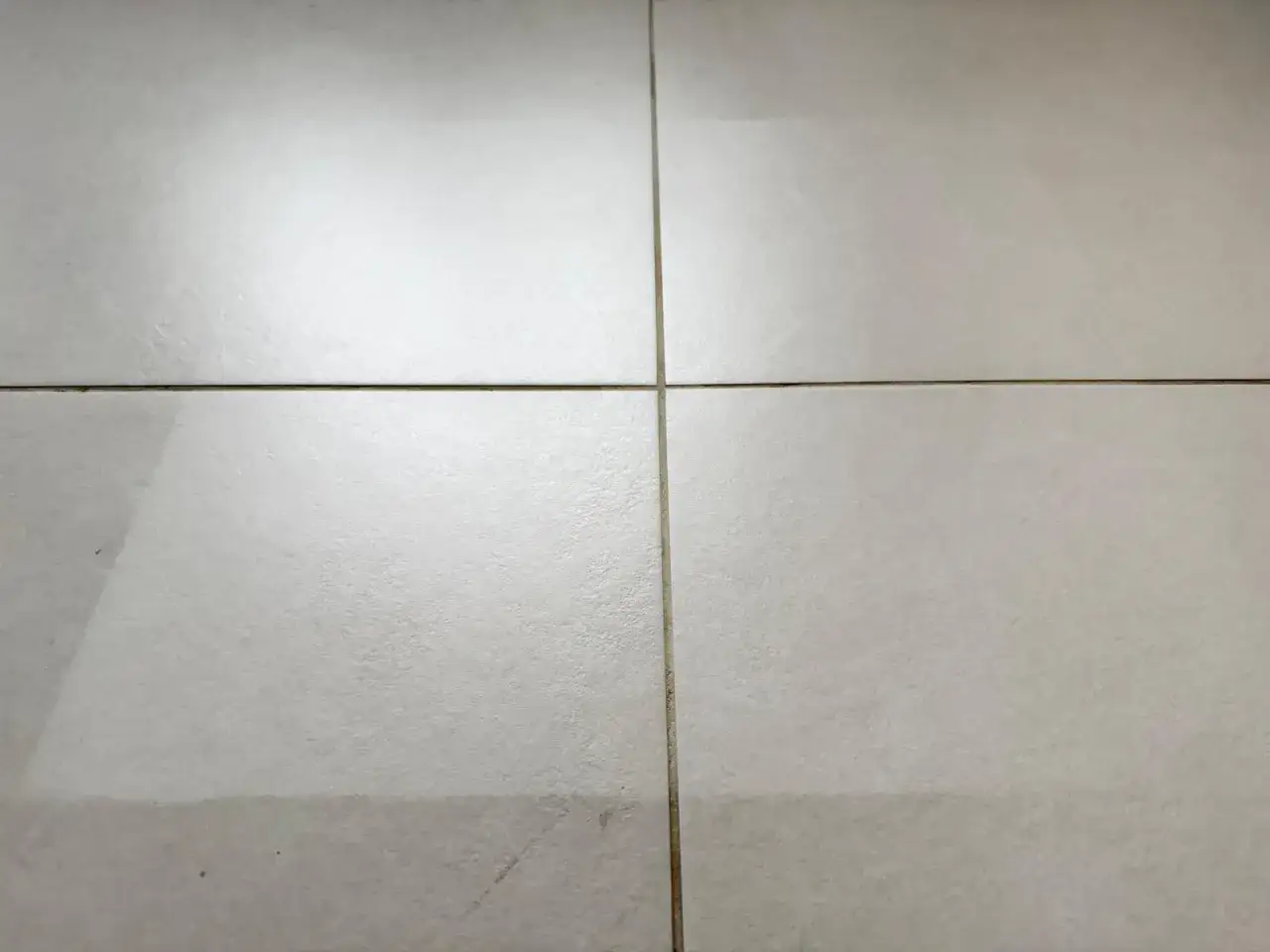 Pavimento in piastrelle chiare con fughe sottili. Una leggera patina bianca suggerisce la necessità di pulizia per farle risplendere.