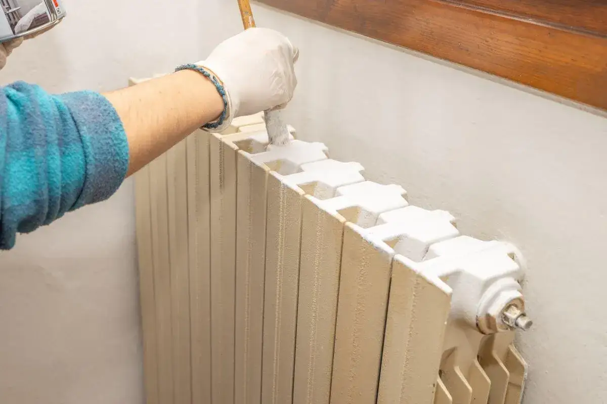 Mano guantata che usa un pennello per verniciare termosifoni, dando nuova vita a un elemento della casa.