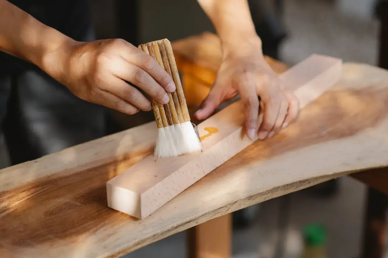Mani che applicano colla su un pezzo di legno con un pennello. Un metodo per come togliere la colla dal legno.