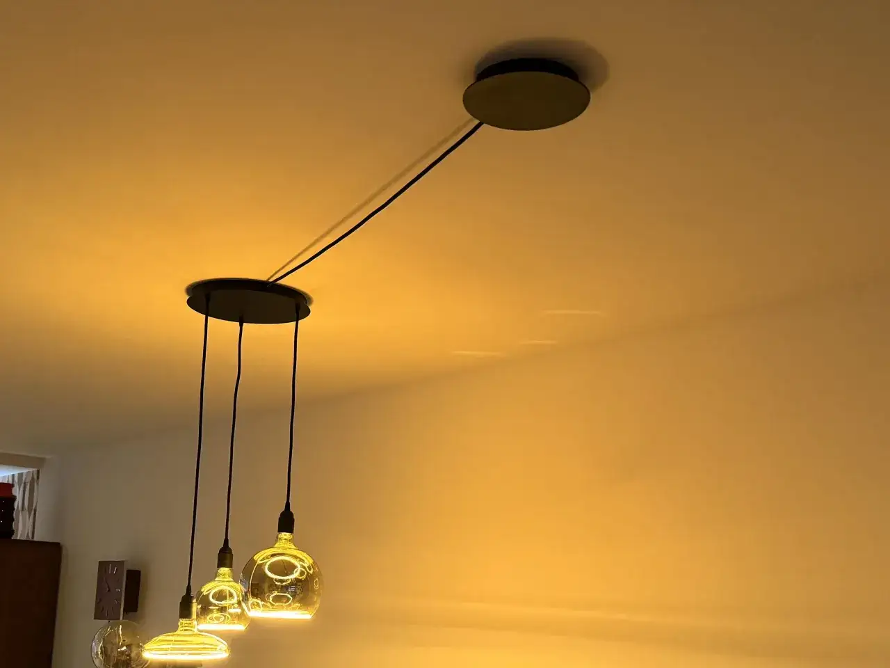 Spostare punto luce soffitto: lampadario moderno con tre sfere luminose e cavi neri che si collegano a un rosone sul soffitto.