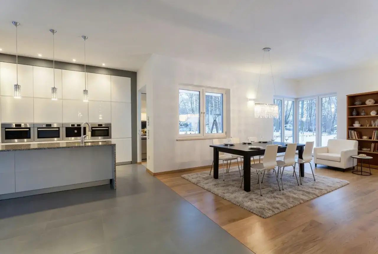 Cucina moderna con isola e zona pranzo con tavolo, sedie e un divanetto. Il pavimento unisce eleganti maioliche grigie e caldo parquet.