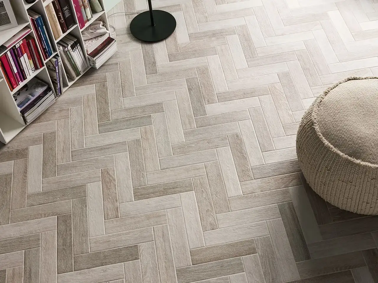 Un elegante pavimento ruvido interno in parquet a spina di pesce, con una libreria e un pouf.
