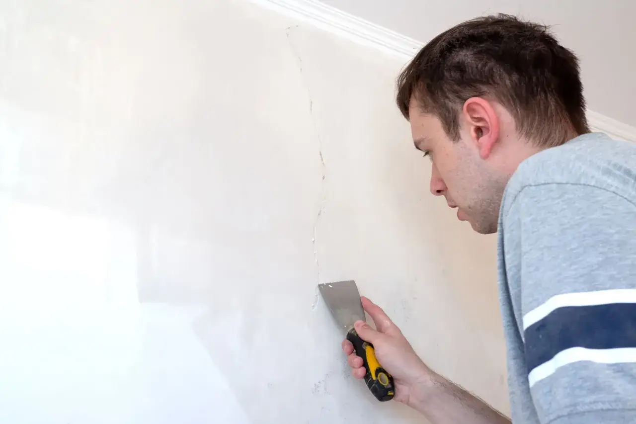 Uomo ripara una crepa su un muro interno, cercando idee per coprire un muro interno rovinato.