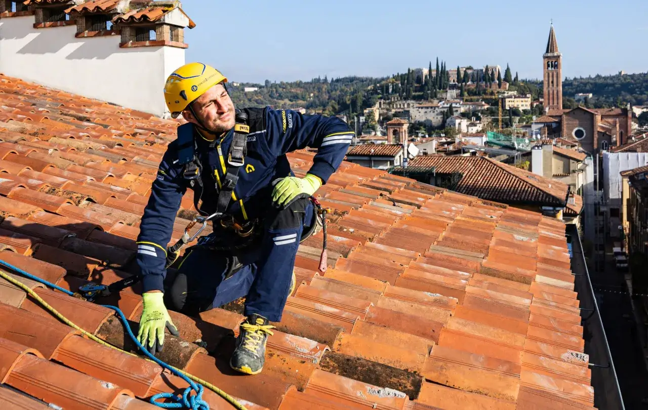 Operaio su tetto in tegole rosse, con vista panoramica sulla citt&agrave;. Valutazione del costo tetto al mq per un lavoro sicuro e di qualit&agrave;.