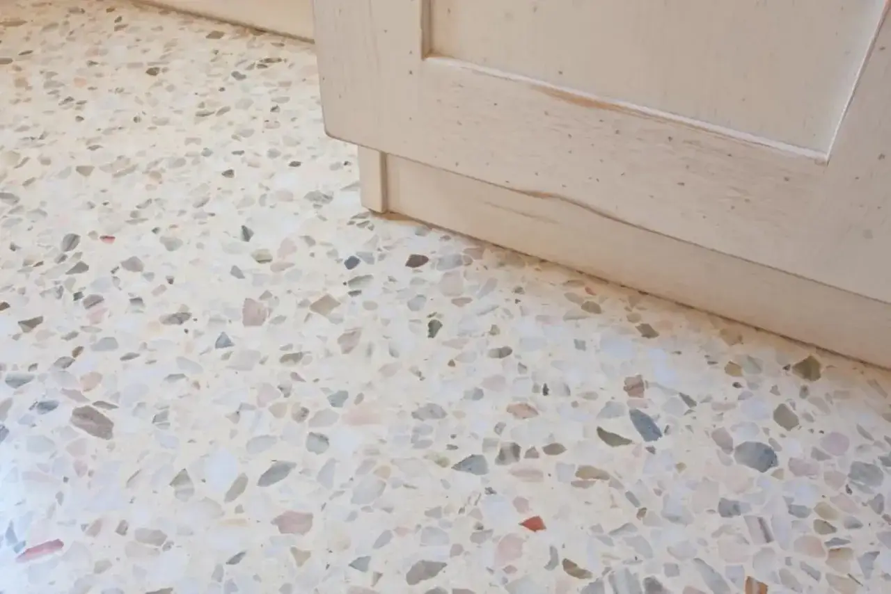 Un elegante pavimento veneziana con schegge di marmo colorate, accanto a un mobile in legno chiaro.